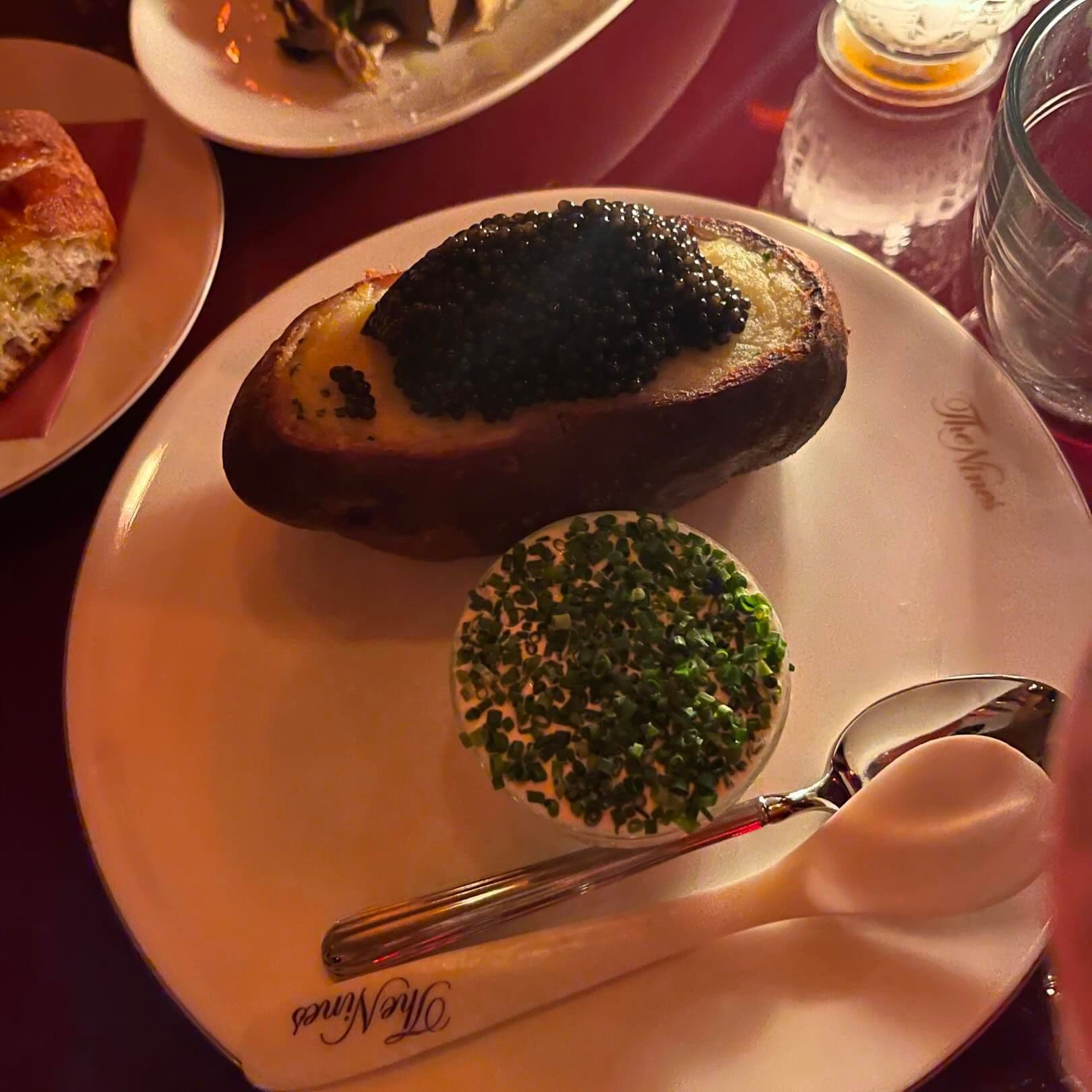 A luxurious baked potato topped with a generous portion of caviar, served with a side of chopped chives, embodying the opulent culinary creations found in New York's premier restaurants booked through Booked.