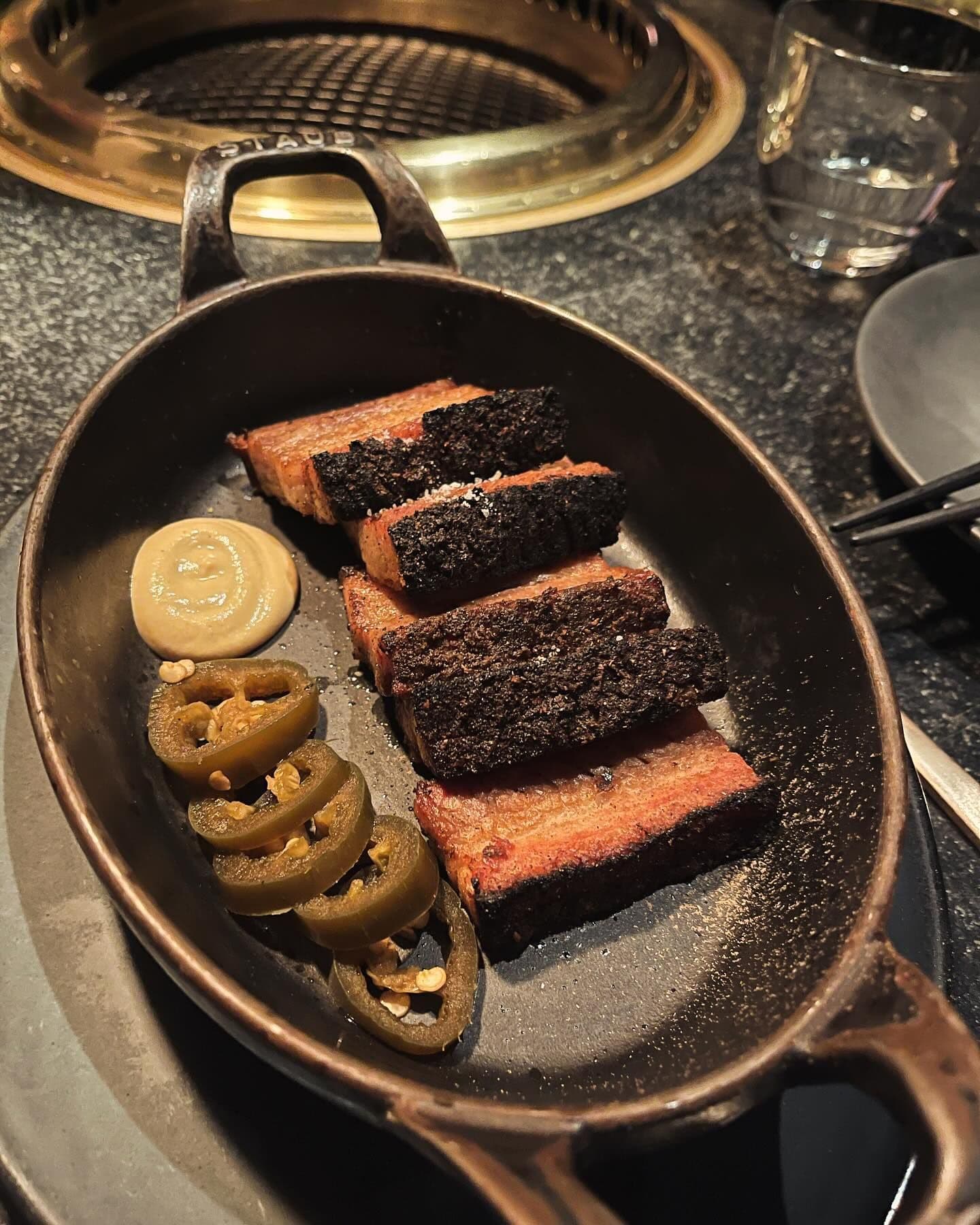 Succulent crispy pork belly slices served in a skillet with sliced jalapeños and mustard, a dish reflecting the gourmet creativity found in New York's top restaurants booked through Booked.