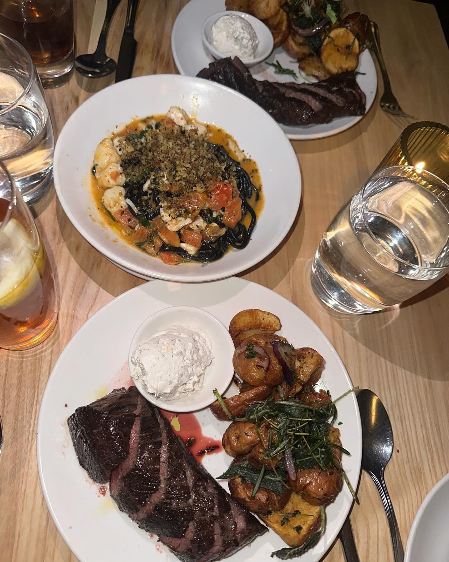 Upscale dining experience featuring a succulent steak, squid ink pasta with seafood, and roasted potatoes, all beautifully presented and ready to be savored in a fine New York restaurant, available for booking through Booked.