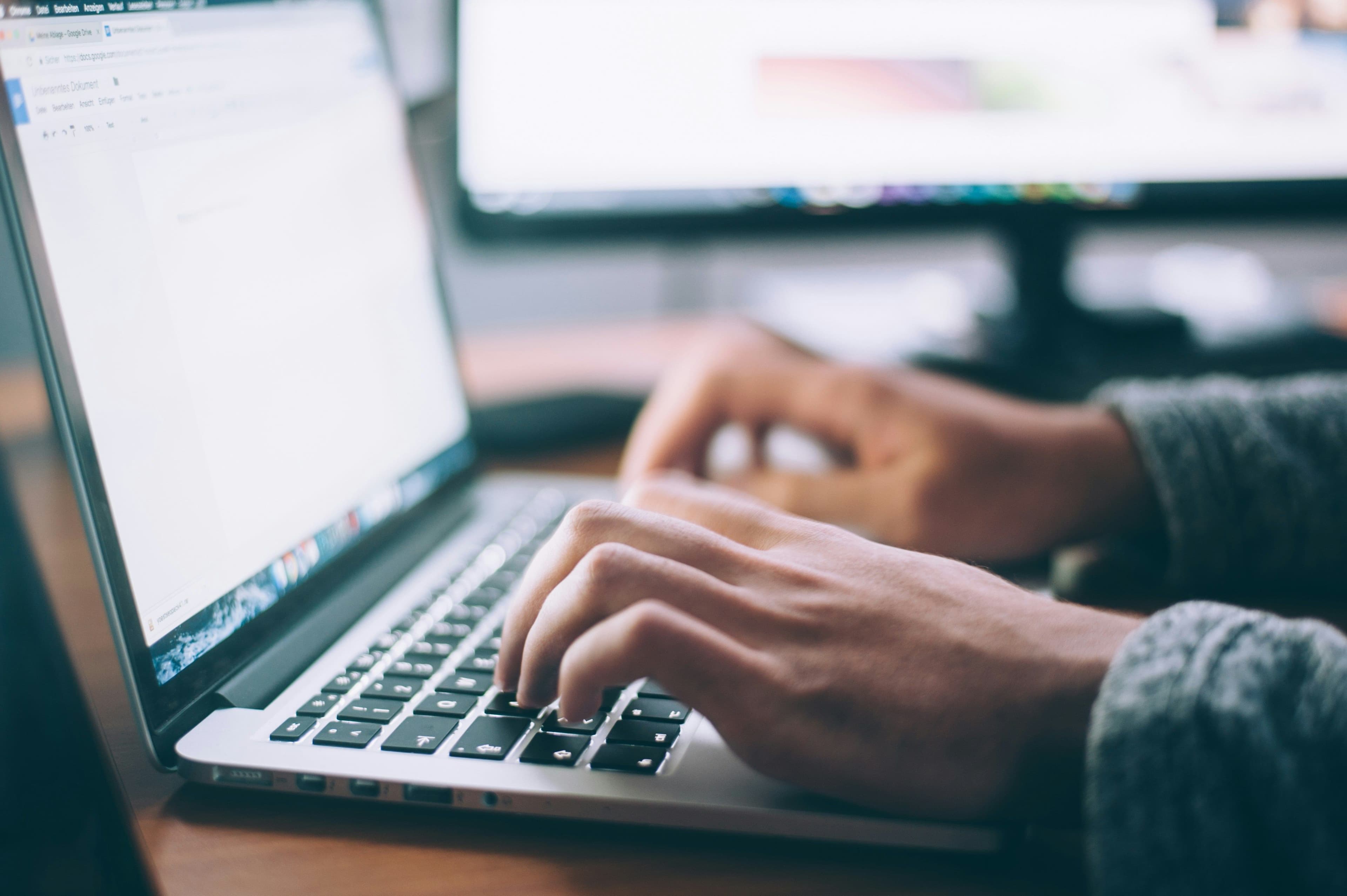 Close-up view of hands typing on a laptop keyboard, indicating a person deeply focused on their work in a bright and modern workspace, possibly researching or booking through an online platform.